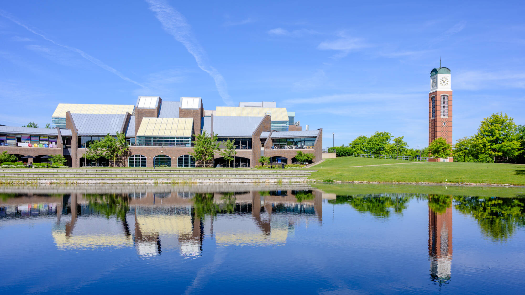 On the warm morning of May 29, the Russel H. Kirkhof Center and the Cook Carillon Tower are reflected on Zumberge Pond.